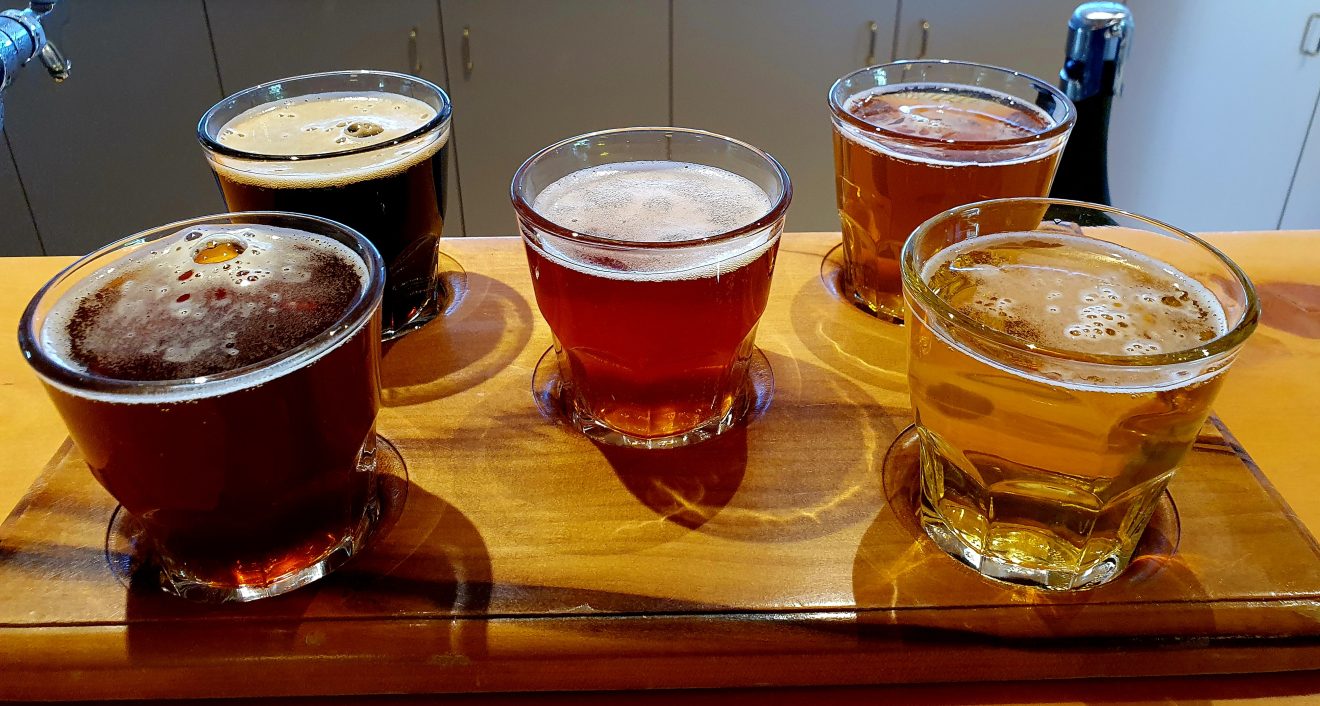 Five small glasses of different coloured beers on a tasting paddle